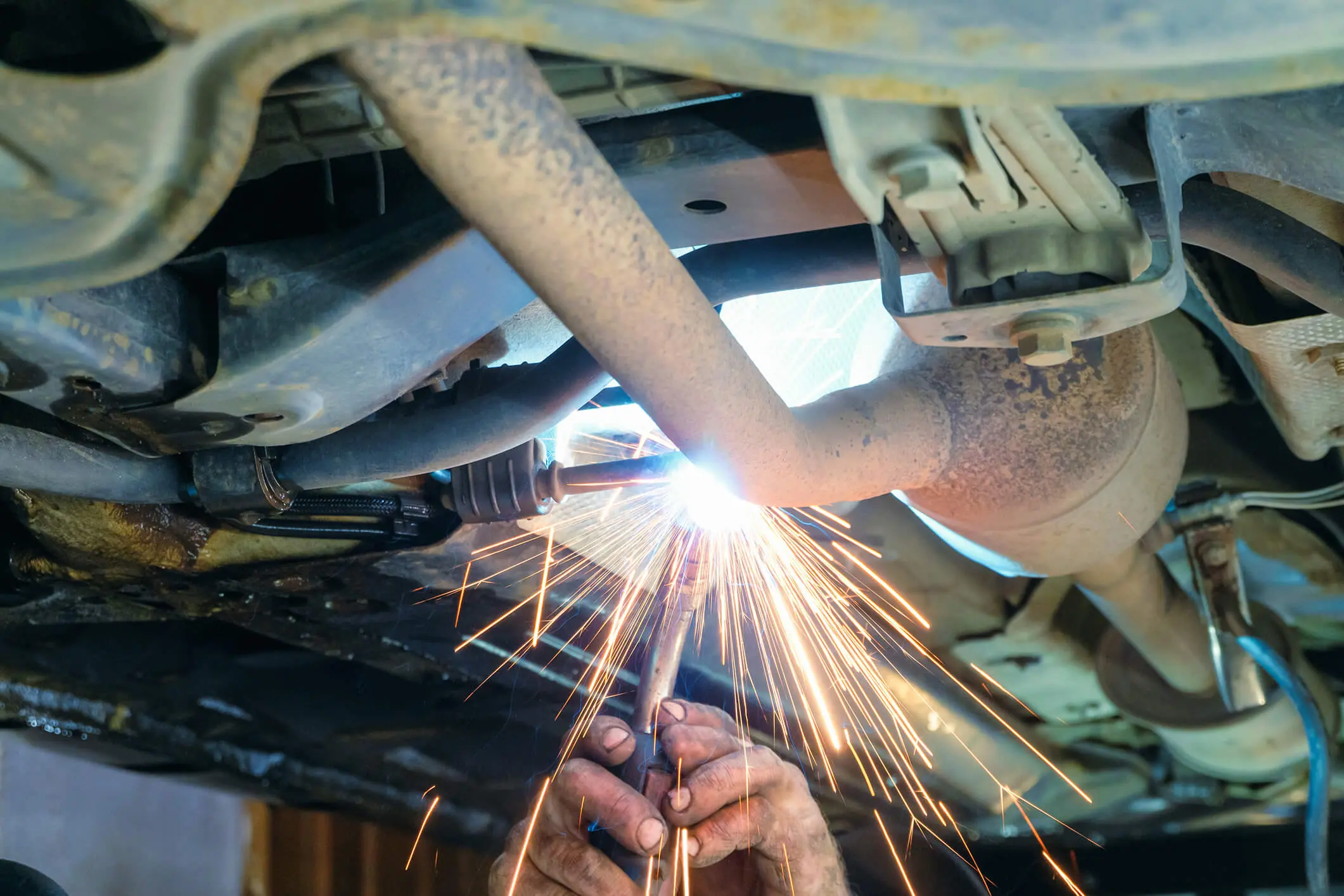 Welding sparks under a car exhaust system.